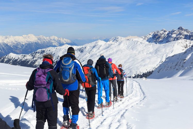 Group of people hiking on snowshoes and mountain snow panorama with blue sky in Stubai Alps, Austria Sellrain, Austria - February 11, 2017: Group of people hiking on snowshoes and mountain snow panorama with blue sky in Stubai Alps. Snowshoeing is a very popular sport in the Alps during winter.